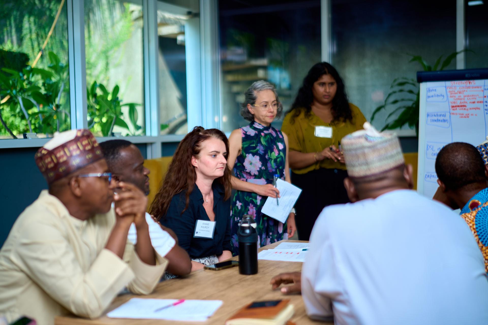 A group of people sit around a table during a meeting. The group includes men and women from different nationalities.
