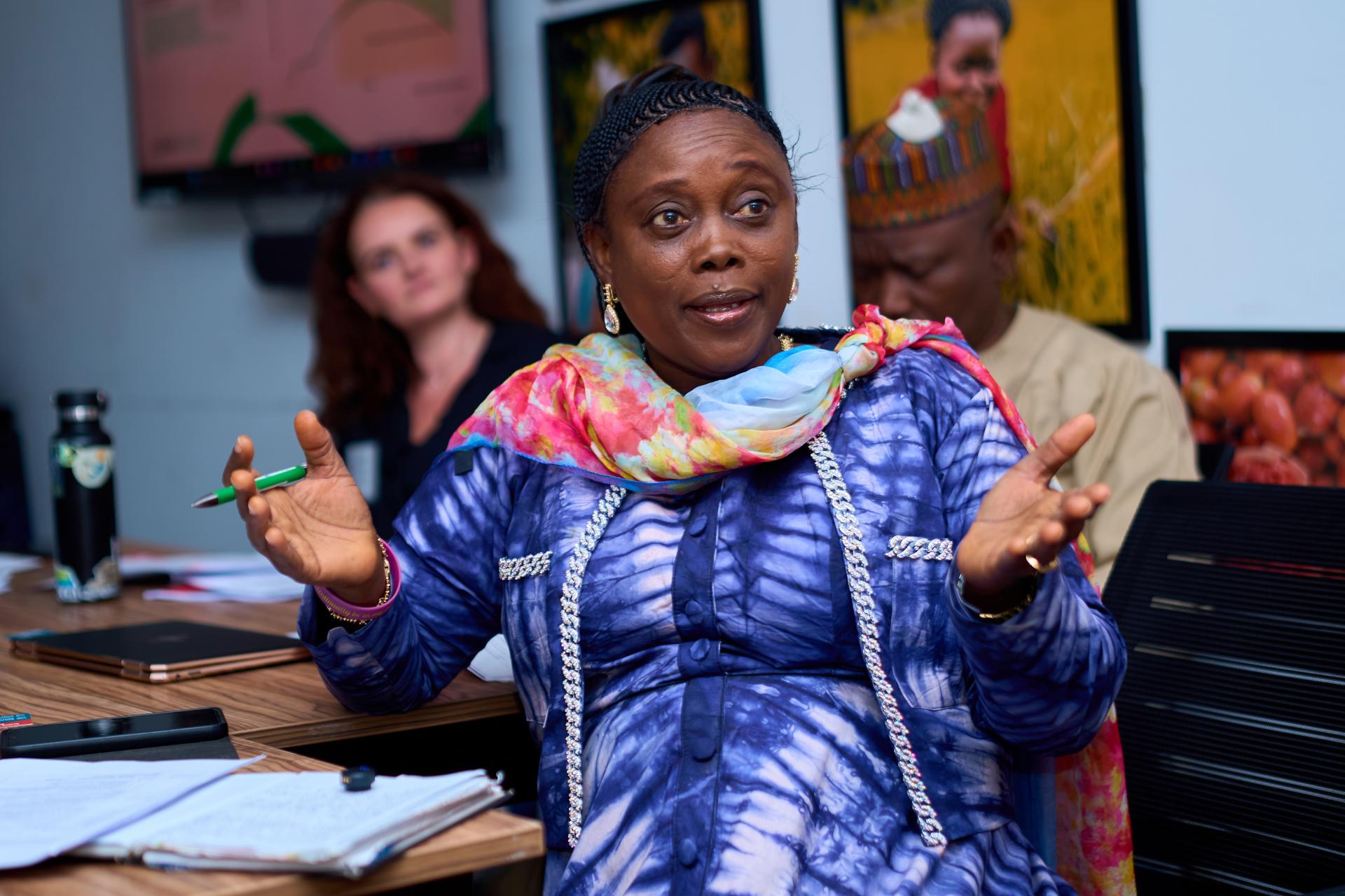An African women in a purple dress speaks while gesturing with her hands.
